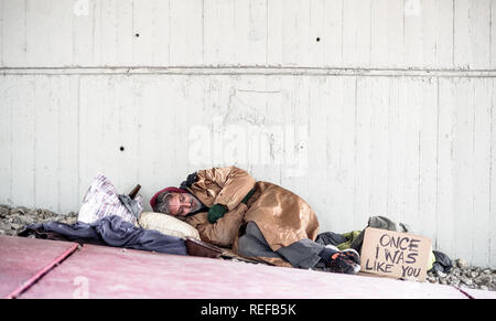 Homeless beggar man lying on the ground outdoors in city, sleeping. Copy space. Stock Photo