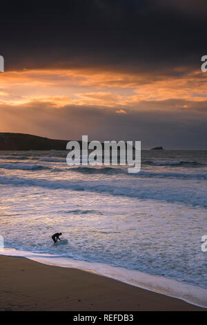 A spectacular sunset as a lone surfer stands in the sea on Fistral Beach in Newquay Cornwall. Stock Photo