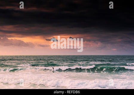 A spectacular sunset as a lone surfer rides a wave at Fistral Beach in Newquay Cornwall. Stock Photo