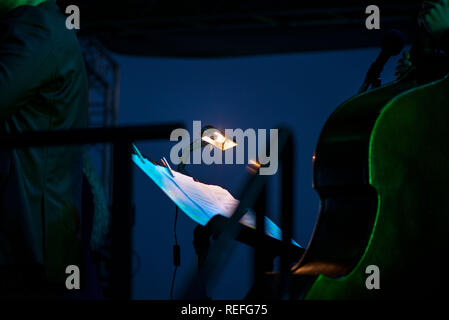 Music sheets and notes on stand, next to microphone. Artists and musicians in background preparing for performance. Classical instruments. Concept of Stock Photo