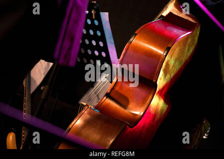 Wooden cello or violin on stage prepared for playing. Music sheets and notes on stand. Classical instruments. Concept of orchestra music. Audience wai Stock Photo
