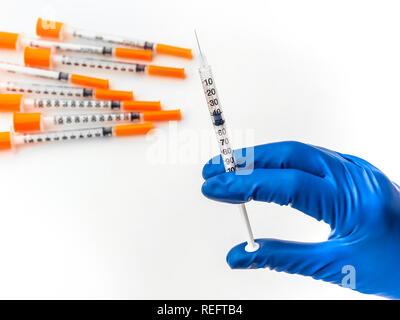 Doctor's hand in blue medical glove holding syringe with medical solution. Several empty syringes are nearby on white isolated background. Flu vaccine Stock Photo