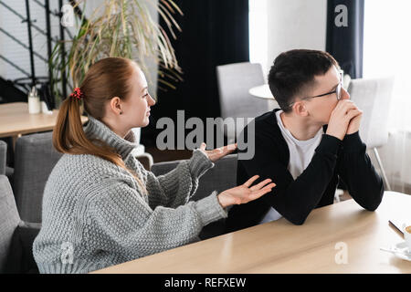 Unhappy young couple arguing, angry wife looking at husband blaming him of problems, conflicts in marriage, bad relationships, man and woman having quarrel or disagreement Stock Photo