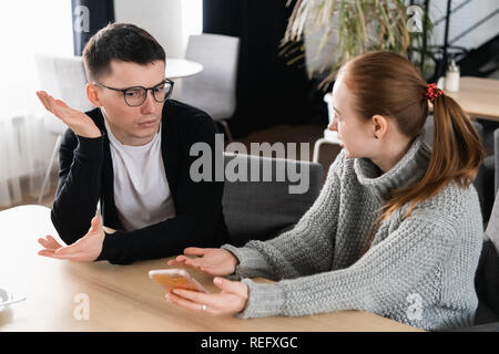 Girlfriend asking for explanation of her boyfriend sitting on a couch in the cafe Stock Photo