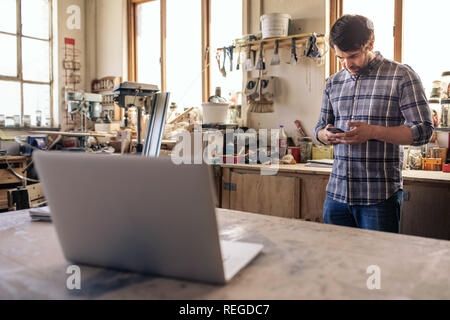 Woodworker reading a cellphone text while working in his studio Stock Photo