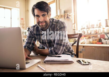 Smiling woodworker using a laptop in his workshop Stock Photo