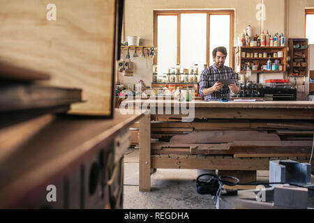 Woodworker using a tablet while sitting at his workbench Stock Photo