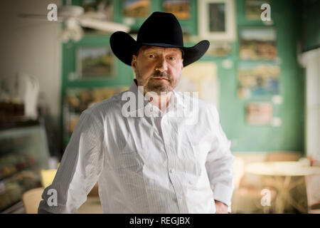 Portrait of a mid-adult bearded man wearing a black cowboy hat and button down shirt while standing inside his home. Stock Photo