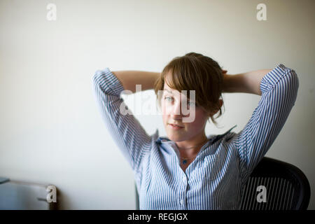 Portrait of a young office worker sitting with her arms behind her head. Stock Photo