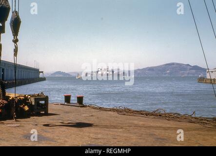 View of the San Francisco Bay and Alcatraz Island from dock near Hyde Street pier and Embarcedero neighborhood of San Francisco, California, now Fisherman's Wharf, with sailboat passing the island, 1945. () Stock Photo