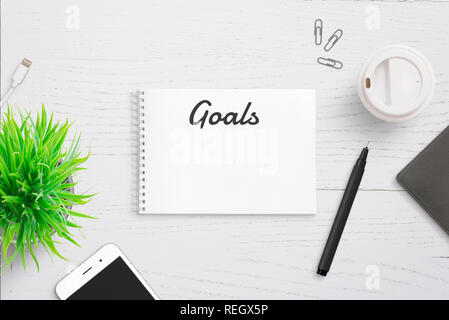 Goals text on notepad page header. Annual writing list. Smart phone, pencil and coffee beside. Stock Photo
