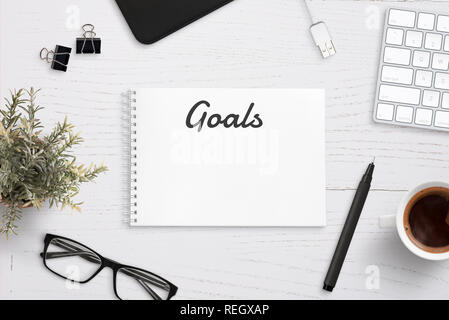Creating goals list on notepad on office desk surrounded with office supplies. White wooden work desk. Stock Photo
