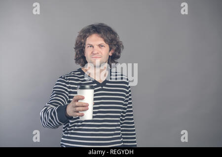 Portrait of happy handsome dark haired curly man in striped sweater with paper cup of morning coffee isolated on grey background. Good morning with te Stock Photo