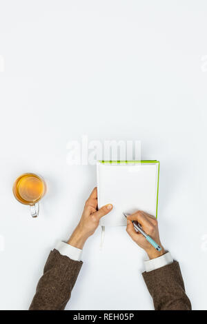 Writing in a note pad, top view. Male person's hands taking notes in a copy book in white background with vertical copy space Stock Photo