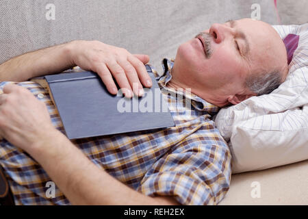 Senior man sleeping on sofa with a book Stock Photo