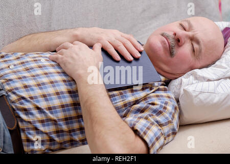 Senior man sleeping on sofa with a book Stock Photo