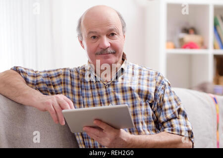 Senior man using tablet sitting at home. Stock Photo
