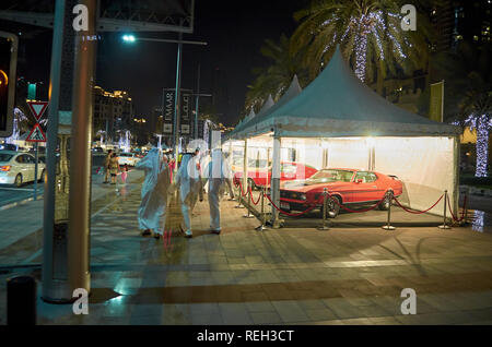 Night life in Dubai city. Arab men walking wearing kandoras, luxury cars parked and illuminated trees decorate the amazing city center of Dubai, Unite Stock Photo