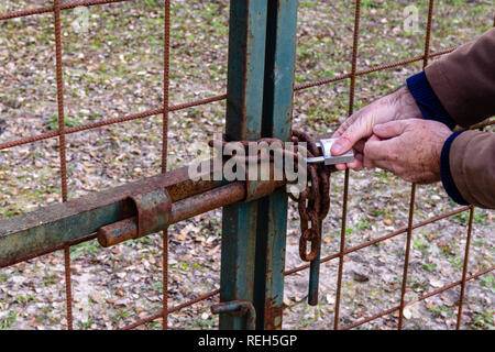 Unlocking padlock on the gate of rusty metal steel Stock Photo