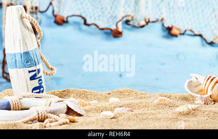 Nautical still life on beach sand over a blue wood background with a life ring, buoy, and scattered seashells around central copy space Stock Photo