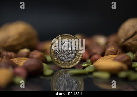 One pound British sterling coin surrounded with variety of nuts, including walnuts, hazelnuts, almonds and pumpkin seeds in the black background Stock Photo