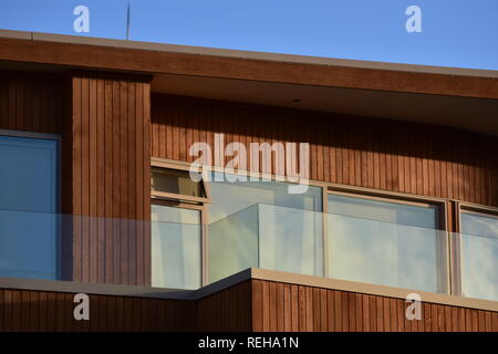 Facade with windows and veranda of modern wooden house with vertical varnished cladding and glass transparent railing. Stock Photo