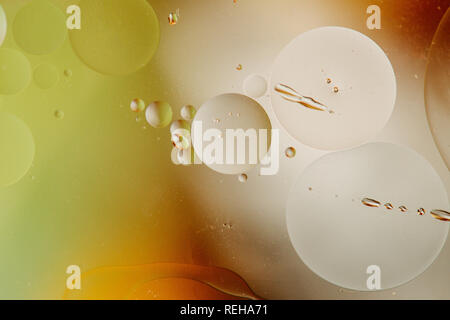 Macro shot of backlit water-oil emulsion over colored background. Tiny gas bubbles inside larger oil bubbles inside water base. Drops of water and scr Stock Photo