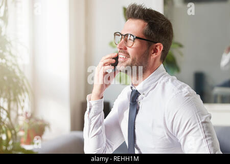 Close-up portrait shot of handsome businessman wearing shirt and tie while sitting in the office and talking with somebody on his mobile phone. Stock Photo