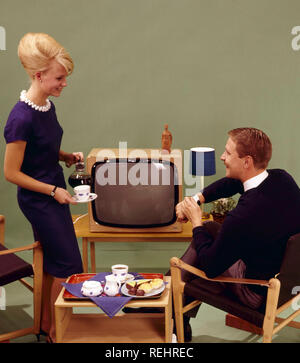 Coffee in the 1960s and fika time. A woman is pouring coffee for her husband in front of the tv set. She has her hair in the typical Beehive hairstyle, in which her long hair is piled up on the top of the head and giving some resemblance to the shape of a traditional beehive. The chairs are of the Safari design type. Sweden 1960s Stock Photo