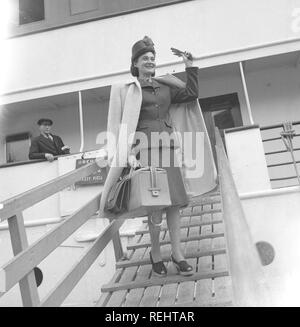 Women's fashion in the 1940s. A young woman in a typical 1940s jacket and skirt, with matching hat, shoes, gloves and handbag. She waves at someone waiting for her on the quay when arriving after travelling with a passenger ship.  Photo Kristoffersson Ref V77-1. Sweden 1947 Stock Photo