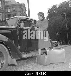 Women's fashion in the 1940s. A young woman in a typical 1940s coat. She has just stepped out of a taxi and pays the driver.  Photo Kristoffersson Ref V77-3. Sweden 1947 Stock Photo