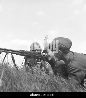 The Regiment's day in the 1940s. A fashionable looking lady is behind a machinegun together with two soldiers. She aims carefully, closing one eye. Sweden 1942 Photo Kristoffersson C20-3 Stock Photo