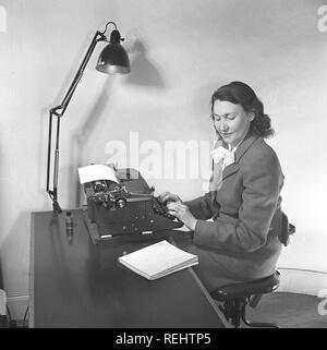 Office girl in the 1940s. A woman is sitting at a office desk typing on her typewriter a text from anotebock. She reads the horthand notes she has written, perhaps with notes from a meeting or a content of a letter to send. Sweden 1948. Photo Kristoffersson AG21-8 Stock Photo