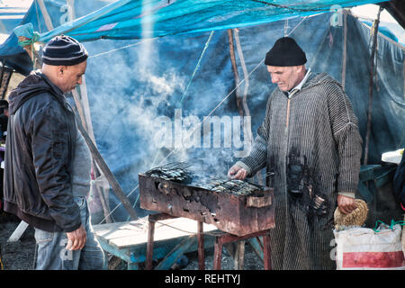 Oued Laou, Chefchaouen, Morocco - November 3, 2018: A man with typical Moroccan attire, roasting sardines in the typical street market Stock Photo