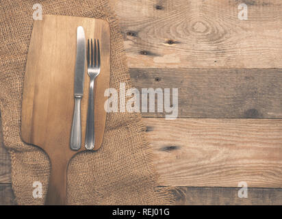 Old used fork and knife and a walnut cutting board on a rustic wooden table with space for your meal Stock Photo