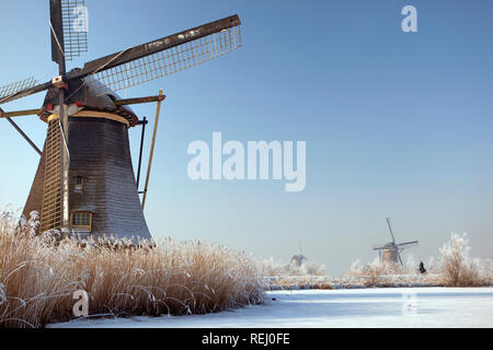 The Netherlands, Kinderdijk, Windmills in snow, Unesco World Heritage Site. Man on bicycle on dike. Stock Photo