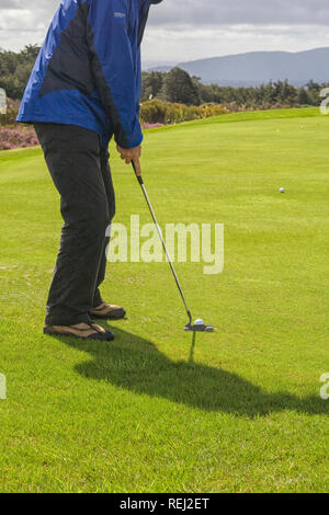 Golfer with putter on the green of a golf course in the rain Stock Photo