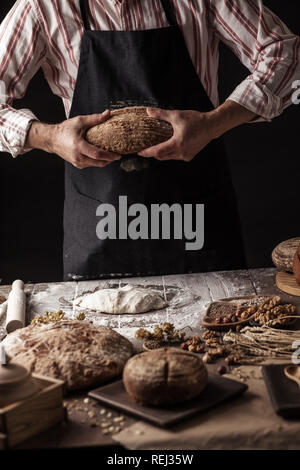Unrecognizable baker holds freshly baked rustic organic loaf of bread in hand Stock Photo