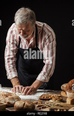 Mature bearded baker man kneading dough for bread on table Stock Photo