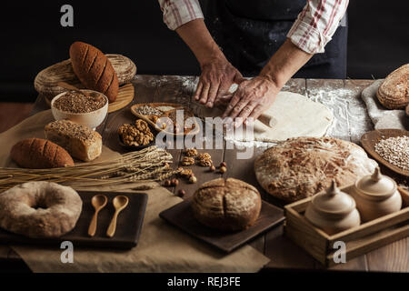 Man rolling out dough on kitchen table, close up Stock Photo