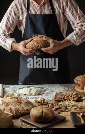 Unrecognizable baker holds freshly baked rustic organic loaf of bread in hand Stock Photo