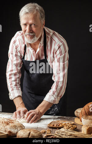 Mature bearded baker man kneading dough for bread on table Stock Photo