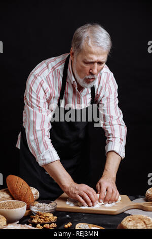 Mature bearded baker man kneading dough for bread on table Stock Photo
