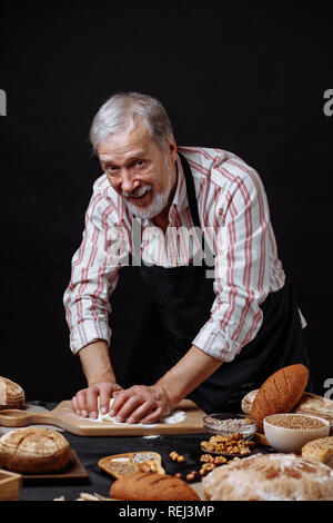 Mature bearded baker man kneading dough for bread on table Stock Photo