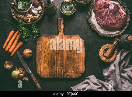 Empty cutting board food background. Rustic table with meat ingredients, vegetables, seasoning and kitchen utensils.  Cooking concept. Top view. Frame Stock Photo