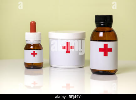 Three assorted medicine containers for dispensing medication with a dropper bottle, plastic tub and brown glass bottle labelled with red crosses Stock Photo