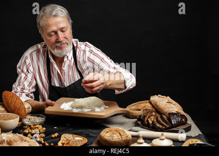 Mature bearded baker man kneading dough for bread on table Stock Photo