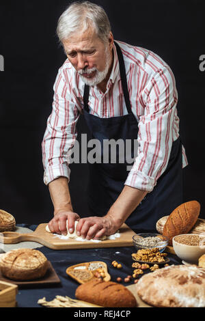 Mature bearded baker man kneading dough for bread on table Stock Photo
