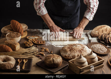 Man rolling out dough on kitchen table, close up Stock Photo