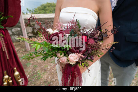 the bride holds a dark red wedding bouquet in her hands Stock Photo